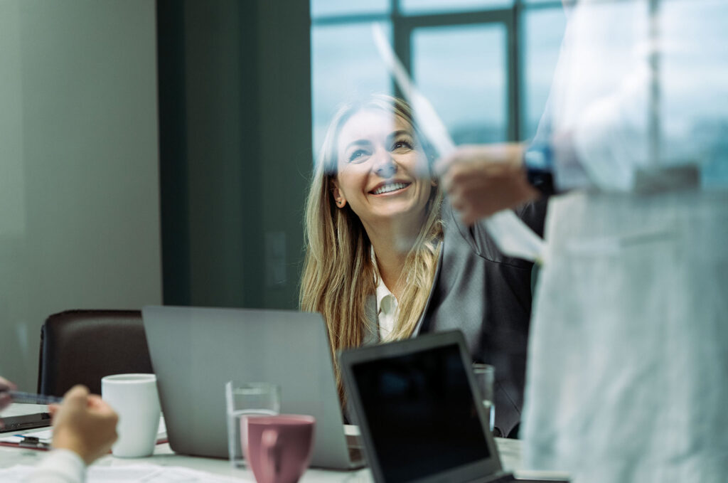 E-Learning kursus i projektledelse. Kvinde smiler op på person, der fremlægger.