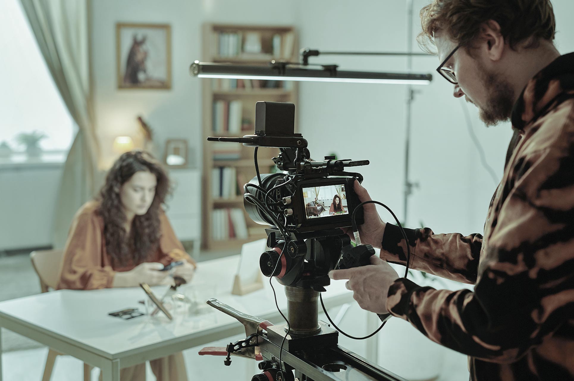 Behind the scenes of a video production for an E-Learning. Man behind camera recording woman at table.